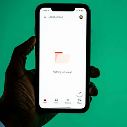 Hand hält Smartphone mit geöffneter Gmail-App vor grünem Hintergrund.